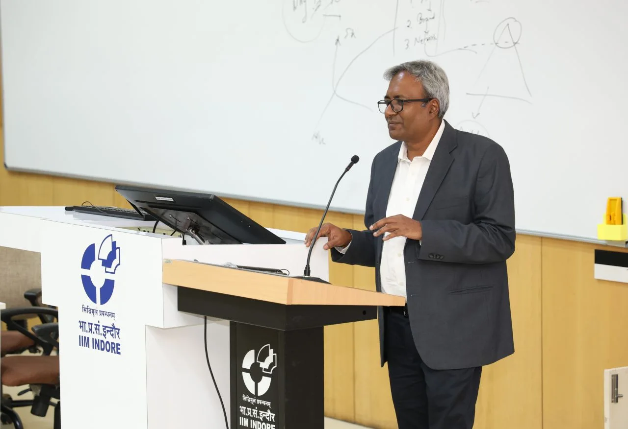 Speaker addressing an audience from a podium with the IIM Indore logo at an alumni event.